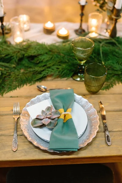 celebration, new year, feast concept. wooden table decorated burning candles of various forms and sizes, fresh green conifer branches and aethstetic beautiful tableware