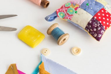 Dikiş, yama işi, terzilik ve moda konsepti - stüdyodaki beyaz masanın üzerine yakın çekim araçları, iğnelik, mavi ve pembe iplik makaraları, beyaz düğmeler, makas, sabun, renkli kumaş parçaları.