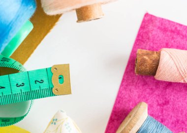 yama işi, dikiş ve terzilik konsepti - araçlara yakın çekim, ölçüm göstergesi, bobinlerdeki mavi ve pembe iplikler ve beyaz arka planda mor ve hardal rengi yamalar, üst görünüm, düz yatış.