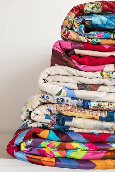 Concepto de costura y moda - pila de primer plano de colchas de colores, hermosas colchas apiladas en varias filas de altura para el almacenamiento, venta de producciones de patchwork sobre fondo blanco, espacio de copia, vertical . — Foto de Stock