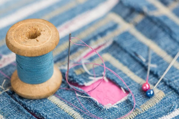 Concepto de costura y bordado - primer plano en carrete de hilos azules, aguja con alfileres sobre tela azul decorada con patrón cortado, macro de costuras y decoraciones de diseño en forma de laberinto . — Foto de Stock