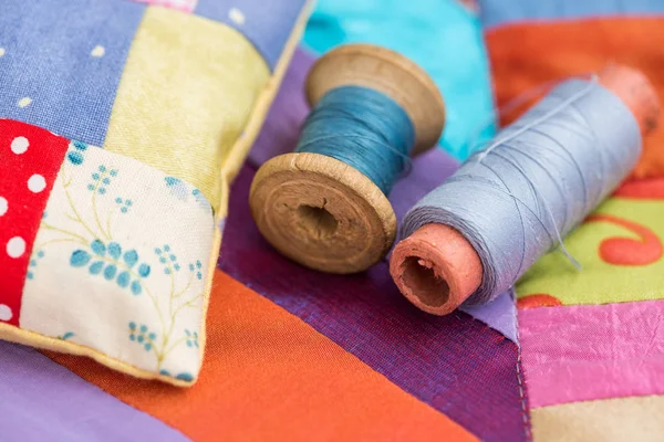 Patchwork, quilting, couture, couture et concept de mode - gros plan sur beau coussin cousu coloré et bobines de fil bleu à l'arrière-plan de rabats bleus, lilas et rouges de tissu . — Photo