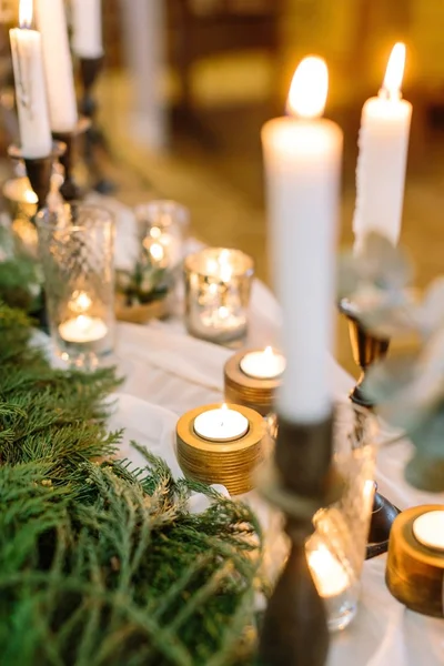 Illumination, comfort, christmas feast concept. table with numerous of candles in various holders made of glass, gold, wood, all of them placed on the edge by fresh fuzzy conifers branches — Stock Photo, Image