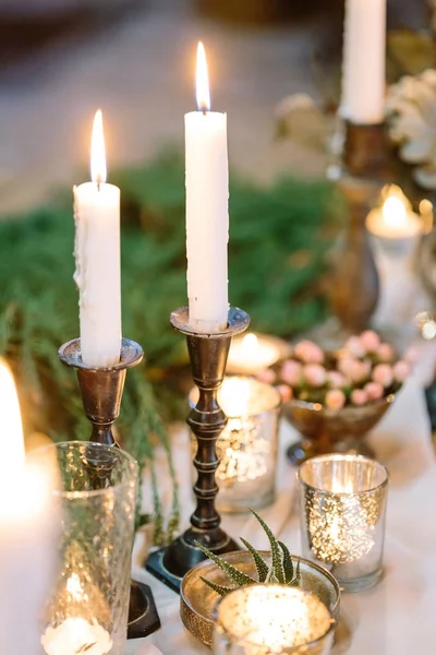 comfort, cosiness, entertainment concept. two tall white candles are burning in their holders, surrounded by different small ones, there is wonderful tableware