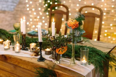 Noel, kutlama, tasarım konsepti. Narin çiçeğe yakın, narin turuncu renkli gül tomurcuğu, bir sürü mum, lamba, bardak ve ladin dallarıyla çevrili.