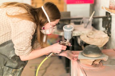 El işi, hobi, profesyonel konsept. Uzun saçlı, orijinal küpeli ve dövmeli tatlı bir kız seramik kasesine parlak gri bir jöle sürüyor.