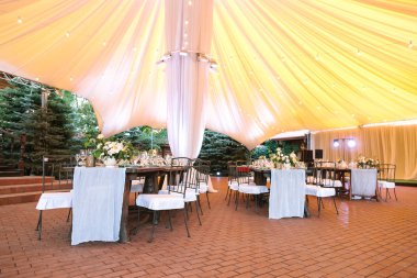 Restoran, nişan, iç kavramı. vintage tarzı ile dekore edilmiş ahşap masa vardır büyük sarı çadır altında karlı beyaz sofra ve Çiçek demetleri