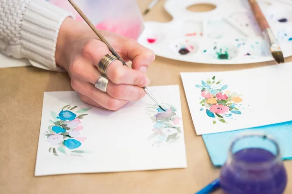 Basteln, Malen, Hobby-Konzept. Nahaufnahme des weiblichen Arms, der einen dünnen Pinsel hält und Blumen auf das schwere Papier zeichnet, das ziemlich rau ist und für Grußkarten verwendet wird — Stockfoto