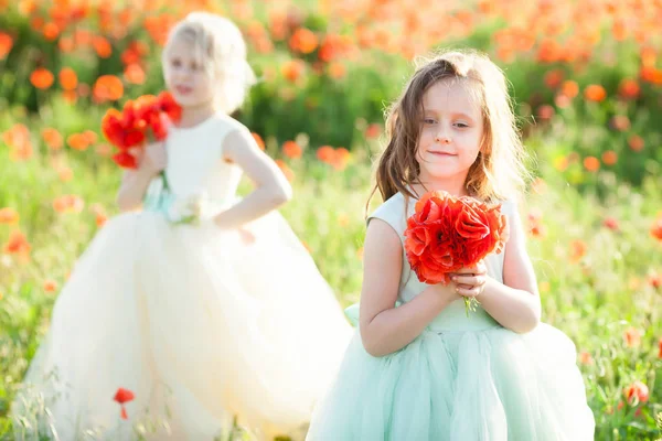 Modelo de niña, la infancia, la moda, el concepto de verano - dos chicas sonrientes modelo en vestidos azules y blancos festivos, reunir ramos de flores amapolas, la segunda chica y la flor en enfoque borroso . — Foto de Stock