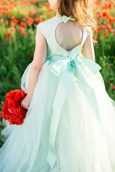 Girl model, wedding, fashion concept - close-up on festive pale blue dress with bowknot and cutout on back of little girl bridesmaid with a bouquet of poppies in hand on the background of poppy field. — Stock Photo, Image