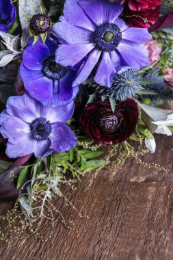 Büyüyen, çiçek aranjmanı, tasarım konsepti. Masanın yüksek desenli ahşap yüzeyinde kan bataryaları ve narin leylak anemonları gibi koyu renk çiçeklerden oluşan bir buket bulunur.