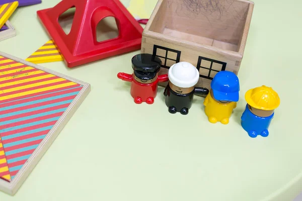 childhood, playing, entertainment concept. close up of four men from lego constructor set of different colour, they are standing nearby small wooden house with painted windows