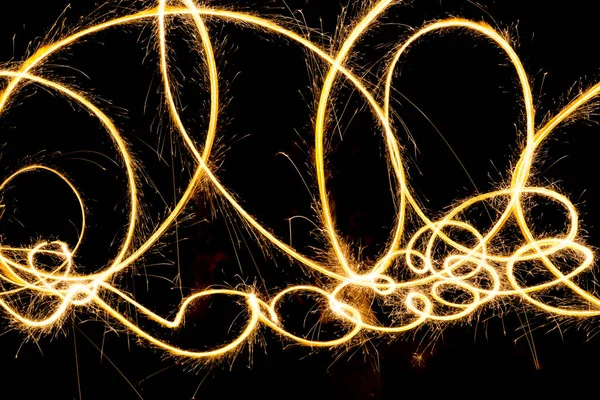 celebration, illumination, amusement concept. golden bright curly line is created with light of firecracker that is used for writting in the air and entertaining guests