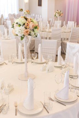 Çiçek aranjmanı, iç mekan, kutlama konsepti. Masanın ortasında beyaz tabaklar ve uzun ve zarif bardaklarla servis edilen harika bir restoran masası var.