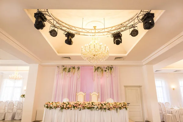 派对概念 大厅中央有一张桌子 供新婚夫妇用 桌子上装饰着华丽的花朵 在这个地方下有漂亮的吊灯和许多聚光灯 — 图库照片