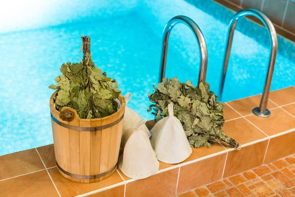 Spa, boş zaman zaman, sağlıklı yaşam konsepti. temiz su ile Yüzme Havuzu kenarında birkaç süpürgeler, beyaz yün şapka ve kova içeren arkadaşlarının banyo ayarla