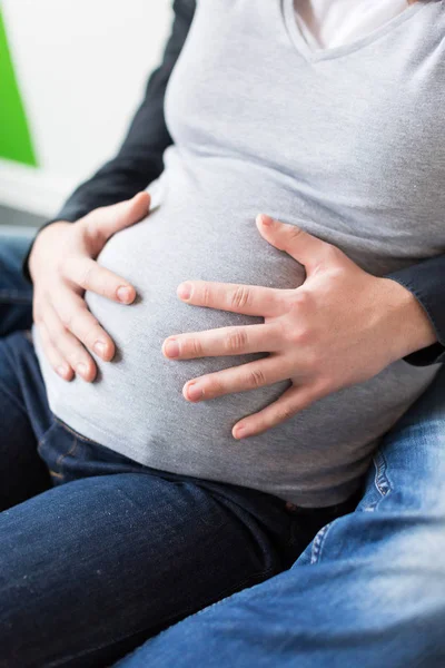 Szerelem, elvárás, amely fogalom születése. közelről a hasa terhes feleségét a férfi fegyverek öltözött szürke pulóver és a szűk farmer, ülnek, átfogó, egymást — Stock Fotó