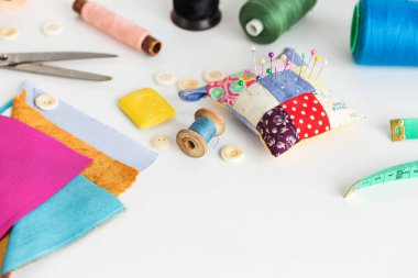 Dikiş aletleri, yama işleri, terzilik ve moda konsepti - stüdyodaki beyaz çalışma masasına yakın çekim, iğne ipliği, iplik makaraları, ölçüm sayacı, düğmeler, makas, sabun, renkli yama kumaşı parçaları.
