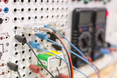 Teknoloji, imalat, cihaz konsepti. Elektronik cihazda çok sayıda bağlantı var, sadece birkaçında iki çoklu metreye giden renkli kablolar var.