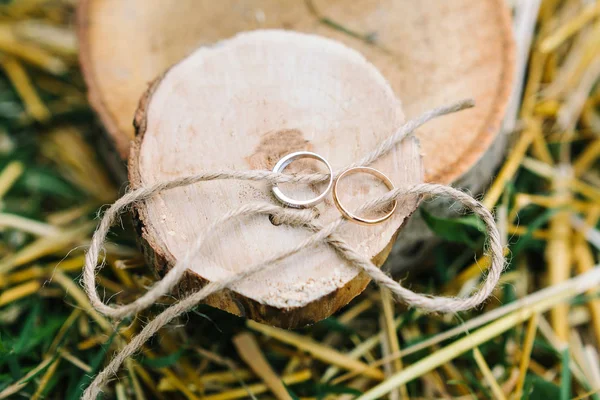 Casamento, acessórios, conceito de jóias. há dois anéis de noivado lindos de prata e ouro nas fatias de madeira das árvores, eles são amarrados com corda áspera — Fotografia de Stock