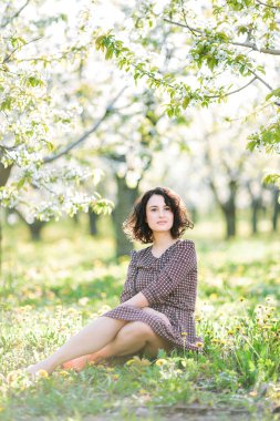 Hava, gezinti, sağlıklı yaşam tarzı konsepti. Taze yeşil çimenlerin üzerinde harika bir kadın var. Güzel elbiseler ve küçük çiçekler giyiyor. Dinleniyor ve yazın tadını çıkarıyor.