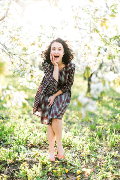 pin up, natural, celebrity concept. concept. there is a charming woman surrounded by blooming apple trees, she looks like black haired marilyn monroe, her radiand smile is shining