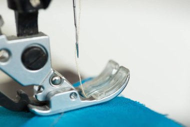 Teknoloji, malzeme, ekipman konsepti. Dikiş makinesinin detaylarına çok yakından bakın. Yüksek kalitede mavi kumaşı geren ince beyaz iplik var.