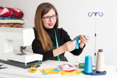 yama, hobi, el işi konsepti. İş yerinde terzi olarak çalışan genç bir kadın var. Yorgan için farklı renklerde yama hazırlıyor.