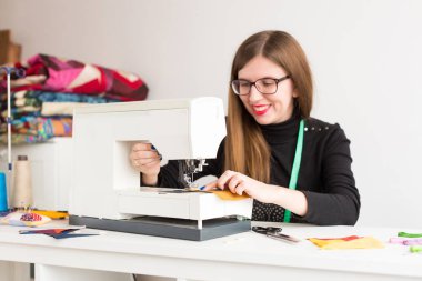 Örtü, ev yapımı, dekor konsepti. Dikiş için hazırlanan atölyede masada oturan ve dikiş makinesiyle çalışan bir kadın var.