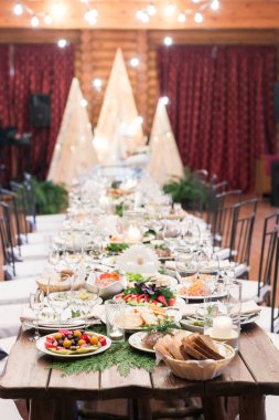Düğün, yemek, gıda kavramı. Gelin ve nişanlısı misafirler için hazırlanan uzun ahşap masanın üzerine bir sürü yemekleri davranır ve şeffaf gözlük parlayan ile