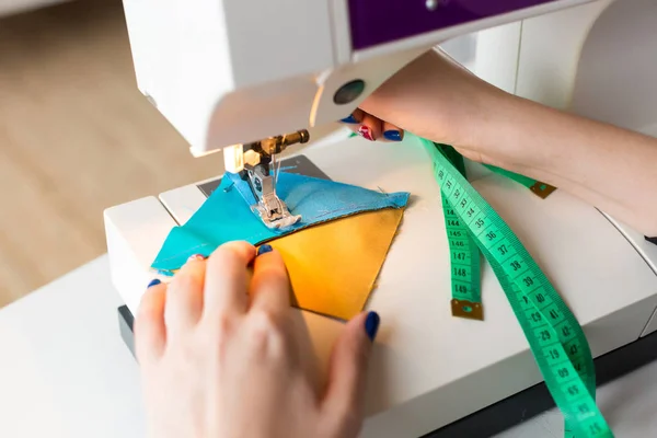 Sömnad, klädsömnad, quiltning koncept. närbild av underbara tekniken utrustning, sömmerska med vacker manikyr använder det för sy gula och blå tyg i ett plåster — Stockfoto