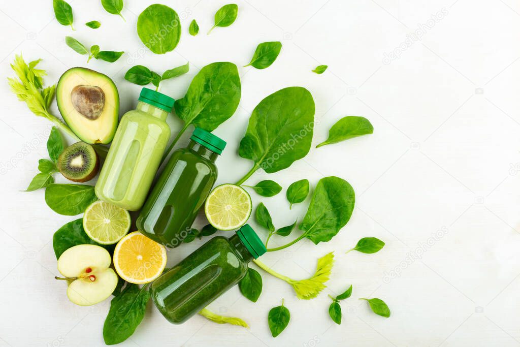 Creatively laid out on a white background set of various detox drinks of different green colours and fresh organic fruits and vegetables for making healthy smoothies. Flat lay, top view.