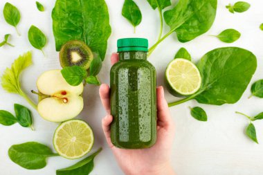 Taze, serin smoothie detoks beyaz arka planda bir kadının elinde yatıyor, turunçgil meyveleri ve ıspanak yapraklarıyla çevrili. Sağlıklı vejetaryen diyet kavramı