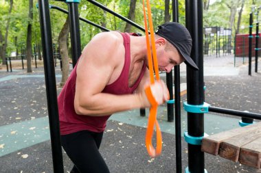 Parktaki spor alanında direniş bandıyla egzersiz yapan kaslı bir sporcu.