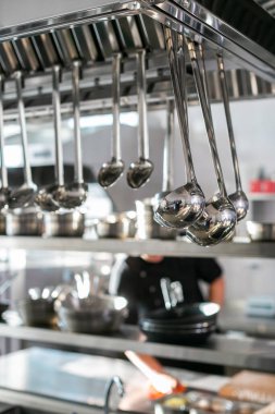 Mutfakta asılı parlak paslanmaz kepçeler. Restoran mutfağı. Parlak kepçeler ve sıra sıra servis kaşıklarıyla.