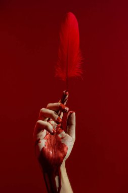 Kırmızıya yapışmış, yapay parlak kanlı ve parlak tüylü bir el.