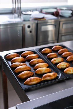 Taze pişmiş turtaların olduğu çarşaflar. Metal tezgahlı fırın mutfağı ve tepesinde altın fırınlanmış turtalar olan tava kağıtları.