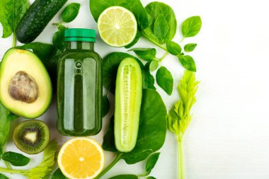 Avokado, ıspanak, salatalık, kivi, limon, kereviz, ıspanak yeşil detoks içeceği şişesinin etrafına serilmiş yeşil sebzeler. Sağlık bakımı ve uygun sindirim kavramı.
