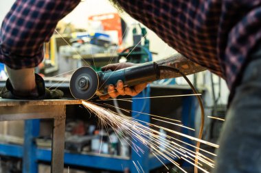 Profesyonel atölyede çalışırken elektrikli testereyle metal kesen yüzsüz bir zanaatkâr.