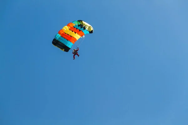 Man soaring in the air currents on a colored parachute against a background of blue. Copy pastre space