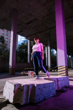 Eşofmanlı bir kadın sokakta taşın üstünde duruyor.