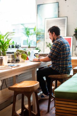 Kahve dükkanında dizüstü bilgisayarla çalışan bir adam. Gündelik modern adam kafeteryadaki ahşap tezgahta oturuyor ve gündüz dizüstü bilgisayar kullanıyor.