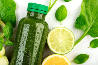 Arınma ve iyileşme için yeşil bir içecekle dolu şeffaf bir şişenin yakın çekimi. Limonlar, limonlar ve ıspanak yaprakları arasında detoks smoothie uzanır.