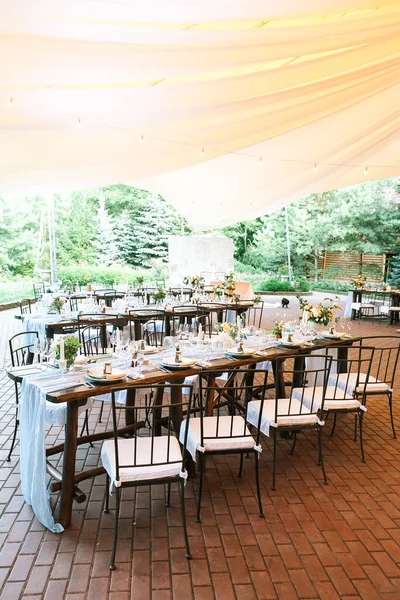 垂直框架 一排排准备好迎接的餐桌和装饰精美的木制餐桌 在一个大帐篷下的婚宴桌上摆满了鲜花和食物 — 图库照片