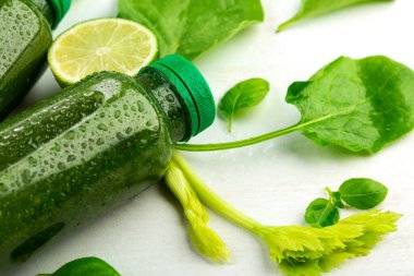 Taze bitki filizleri, bir dilim limon ve beyaz arka planda yeşil içecekle dolu bir şişe. Vejetaryenler için organik gıda konsepti