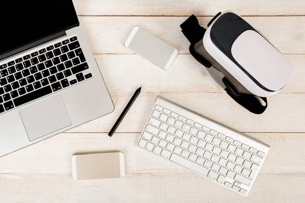 a modern set of devices - laptop, keyboard, electronic pen virtual reality glasses for a young designer or engineer lying on a white wooden workplace. Construction a new augmented reality concept
