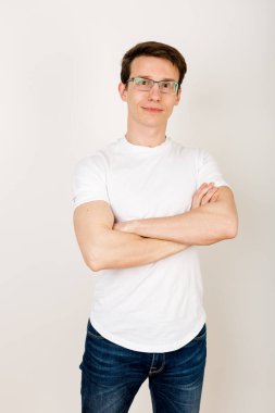 Sıradan giyinmiş genç bir hippi beyaz bir arka planda elleri göğsünde katlanmış ve hafif bir gülümsemeyle kameraya bakıyor..