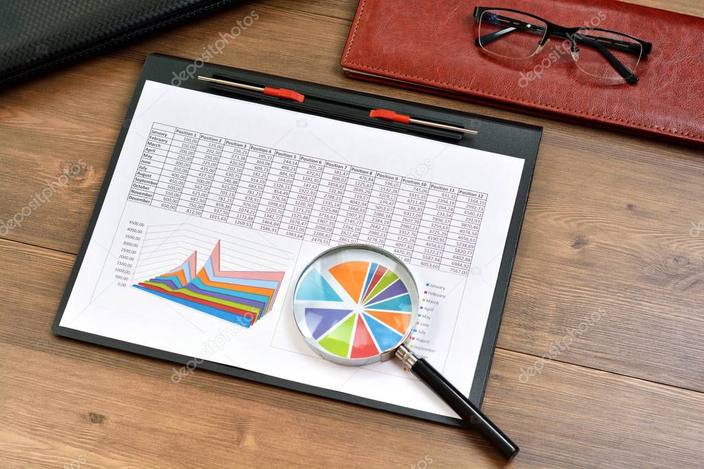 Financial printed paper charts, graphs, diagrams and notebook on a wooden table
