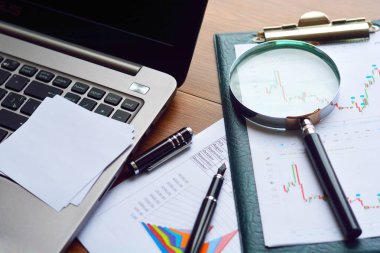 Mali yazdırılan kağıt çizelgeleri, grafikler, diyagramlar, Büyüteç camı, kalem ve ahşap masa üstünde bilgisayar.