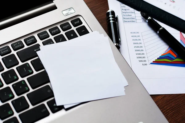 Financial printed paper charts, graphs, diagrams, computer, pen, and calculator on wooden desk.